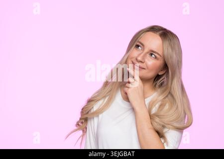 Nachdenkliche junge Frau denkt, lächelt, denkt nach, was sie wählen soll und schaut nach oben Stockfoto