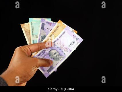 Nahaufnahme einer Hand, die einen Fan gemischter Banknoten aus indischer Rupie vor schwarzem Hintergrund hält, mit 100, 50, 20 und 10 INR-Banknoten Stockfoto