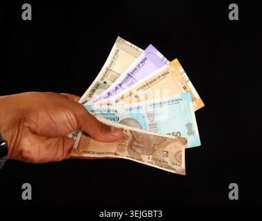 Studio-Aufnahme einer Person, die eine bunte Sammlung verschiedener indischer Banknoten hält, isoliert vor dunklem Hintergrund. Stockfoto