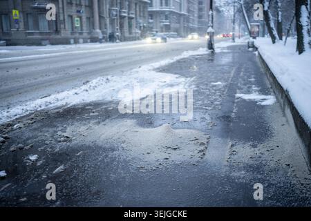 Die Enteisung von Chemikalien auf verschneiten Straßen im Winter. Rutschige Straße mit technischem Salz besprenkelt Stockfoto