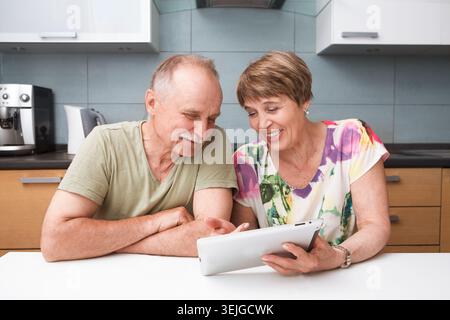 Glückliches Seniorenpaar, das zu Hause ein Tablet in der Küche verwendet Stockfoto