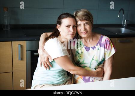 Süße junge Frau und ihre Mutter, die sich in der Küche umarmen Stockfoto