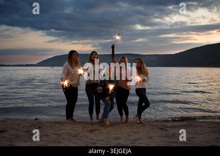 Gruppe glückliche Freunde, die am Strand mit Wunderkerzen feiern. Erwachsenencamp, Wellness-Rückzugsort, Outdoor-Aktivitäten, Stockfoto