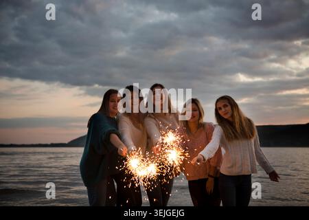 Gruppe glückliche Freunde, die am Strand mit Wunderkerzen feiern. Erwachsenencamp, Wellness-Rückzugsort, Outdoor-Aktivitäten, Stockfoto