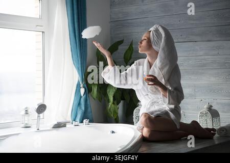Eine junge Frau entspannt sich am Rand des Sprudelbades und trinkt Champagner aus einem Glas zu Hause. Stockfoto