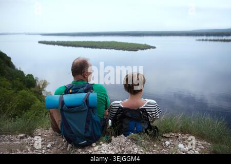 Ältere Ehepaare mit Rucksäcken reisen durch die Berge und ruhen sich aus und genießen den Blick auf den Fluss. Seniorenpaar läuft in nat Stockfoto