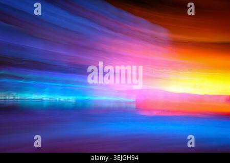 Lebendiges abstraktes Bild mit horizontalen Streifen aus blauem, violettem, orangefarbenem und gelbem Licht, das durch absichtliche Kamerabewegungen erzeugt wird. Stockfoto
