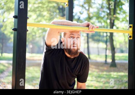 Weißer Mann, der das gelbe Schild beobachtet. Bärtiger Mann mit hellen Augen, der die Aktivität des Parks aufmerksam untersucht. Weißbärtiger Mann, der in Beobachtungshaltung in der Nähe des gelben Warnschilds im Parkszenario steht Stockfoto