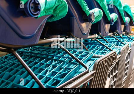 Die Hochwinkelperspektive zeigt eine ordentliche Reihe verschachtelter Einkaufswagen aus blauem Kunststoff mit Kindersitzen aus blauem Stoff und schwarzen Metallrahmen. Stockfoto