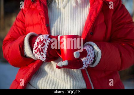 Die Hände der Damen mit warmen Handschuhen halten im Winter einen roten Kakaobecher draußen. Winter Vibes. weihnachtsfeiertage. Kopierbereich Stockfoto