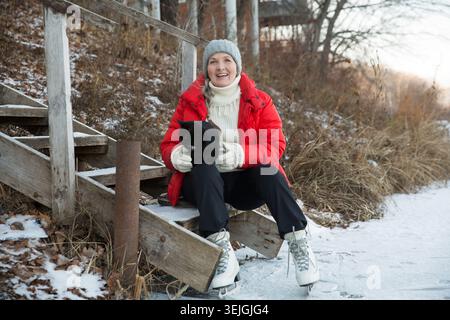 Fröhliche Seniorin Schlittschuhlaufen auf einem gefrorenen See in der winterlichen Natur. Genießen Sie die kleinen Dinge. Winter Vibes. weihnachtsurlaub Stockfoto