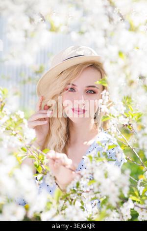 Portret schöne junge Frau in einem Kleid mit Strohhut spaziert im Frühlingsgarten. Stockfoto