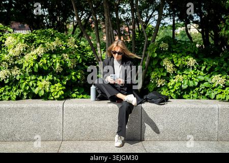 Entspannte, erfolgreiche Geschäftsfrau, die in der Mittagspause im Park sitzt und das Scrollen des Smartphones genießt. Stockfoto