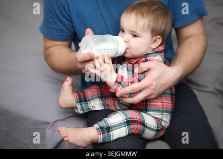 Entzückendes Baby, das Milch aus der Flasche in Vaterhänden trinkt Stockfoto