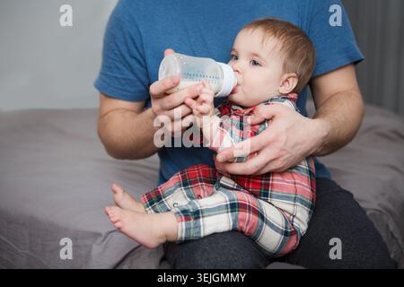 Entzückendes Baby, das Milch aus der Flasche in Vaterhänden trinkt Stockfoto