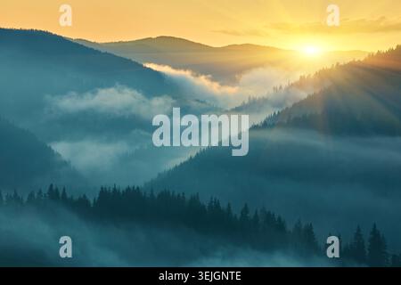 Atemberaubender Sonnenaufgang über Bergschichten, mit hellen Sonnenstrahlen, die durch dicken Nebel in den Tälern dringen. Stimmungsvolle Silhouette der Wildnis. H Stockfoto