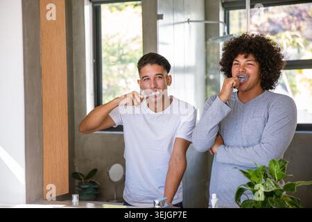 Verschiedene männliche Freunde stehen im Badezimmer zu Hause und putzen Zähne mit Zahnbürsten, Zahnpasta Tube. Freundschaft, Wellness, Hygiene, Entspannung, häusliche umgebung Stockfoto