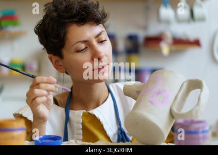 Glückliche konzentrierte Frau malte Tonkrug mit farbenfroher Farbe Formen und Skulpturen Töpfergefäß im Töpferstudio in der Keramikwerkstatt. Mädchenkunst Stockfoto