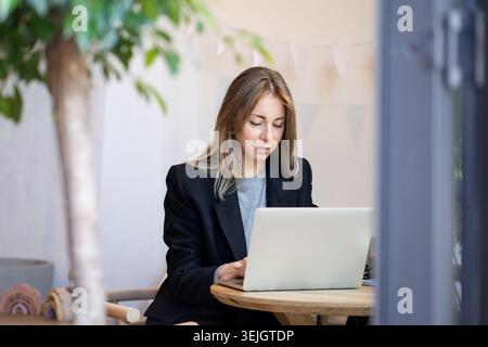 Projektmanagerin, die Arbeitsinformationen auf einem Laptop eingibt, während sie im Café arbeitet. Stockfoto