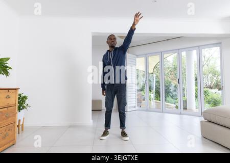Afroamerikaner in 20ern, der im Wohnbereich steht und nach oben zu Glastüren reicht. Person, Zuhause, modern, minimal, hell, i Stockfoto