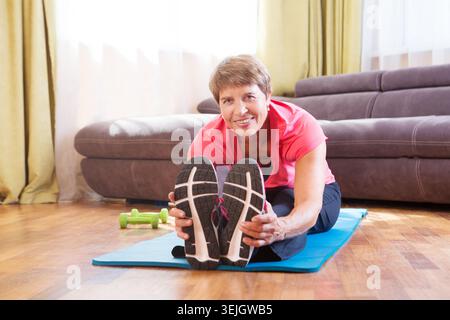 Fröhliche Seniorin, die im Haus Übungen macht Stockfoto