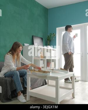 Millennial-Mann und -Frau, die in einem kleinen Büro arbeiten und eine Mittagspause mit Kaffee und Pizza machen Stockfoto