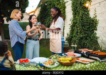 Glückliche, multiethnische Freundinnen, die beim Grillfest im Hinterhof tosten Stockfoto