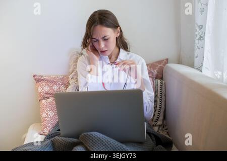 Eine frustrierte Geschäftsfrau, die eine Brille abnimmt, leidet unter Kopfschmerzen, Migräne, die von zu Hause aus auf dem Laptop arbeitet Stockfoto