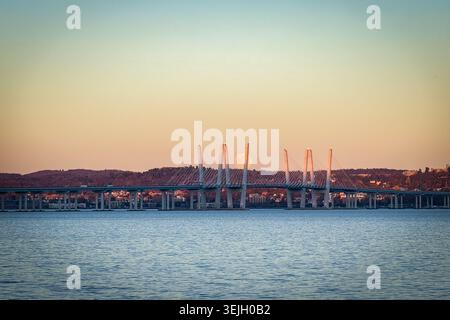 Aus der Vogelperspektive auf die Governor Mario M. Cuomo Bridge, die den Hudson River überspannt, mit einem Vollmond, der bei Sonnenuntergang hinter den Türmen in Sleepy Hollow, New, aufsteigt Stockfoto