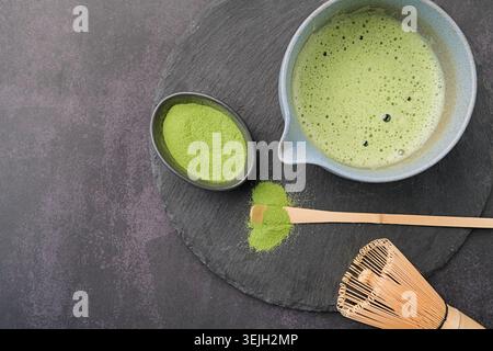 Traditionelles grünes Matcha-Set, Bambusquirl und Getränk auf Schieferplatte, dunkler Hintergrund mit Kopierraum Stockfoto
