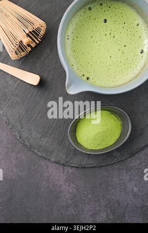 Traditionelles grünes Matcha-Set, Bambusquirl und Getränk auf Schieferplatte, dunkler Hintergrund mit Kopierraum Stockfoto