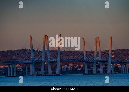 Aus der Vogelperspektive auf die Governor Mario M. Cuomo Bridge mit einem großen Vollmond, der hinter ihren Türmen über den Hudson River in der Abenddämmerung in Sleepy Hollow, New, aufsteigt Stockfoto