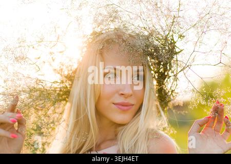 Schöne glückliche junge Dame in einem Kranz aus Sommerblumen über die Natur Stockfoto