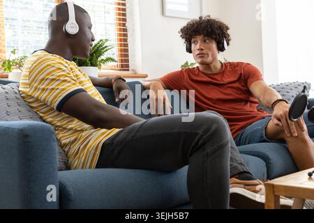 Verschiedene männliche Podcast-Gastgeber verwenden Mikrofon und nehmen Gespräche auf blauem Sofa im Wohnzimmer auf. Studio, Entspannung, modern, Stockfoto