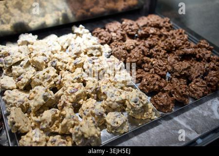 Verschiedene dunkle und weiße Schokoladen-Rock-Clusters mit Nüssen auf Tabletts in einer Bäckereivitrine Stockfoto