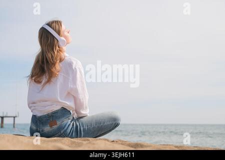 Frau, die Kopfhörer trägt und Musik hört, frische Luft atmet und sich am Strand entspannt Stockfoto
