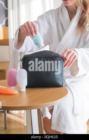 Frauenhände, die kosmetische Reiseausrüstung auf dem Couchtisch halten. Farbenfrohe Kosmetikflaschen Stockfoto