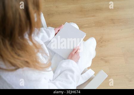 Nicht erkennbare Frau, die ein leeres Buch für das Modell hält, im Hotelzimmer sitzt Stockfoto