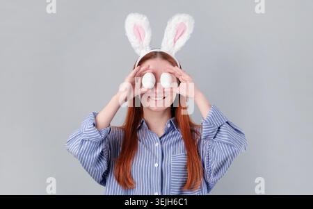 Frau mit Kaninchenohren, die Eier isoliert auf hellgrauem Hintergrund hält Stockfoto