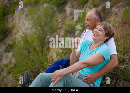 Ein älteres Ehepaar, das auf einem Berg sitzt, bewundert die Landschaft bei Sonnenuntergang. Seniorenpaar spazieren in der Natur. Reisetourismuskonzept. S Stockfoto