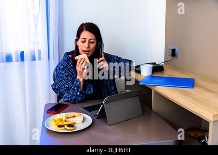 Frau, die per Fernzugriff arbeitet, frühstückt und telefoniert Stockfoto