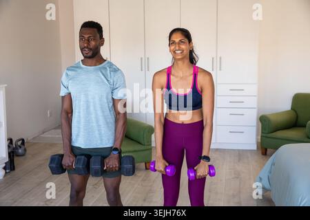 Verschiedene Trainingspartner heben Kurzhanteln im Schlafzimmer mit grünem Sessel mit Kettlebell. Fitness, Workout, Training, Stren Stockfoto