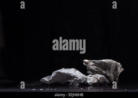Rough natürlichen grauen Stein Podium mit Wasser als Strand in der Nacht für Verpackung und kosmetische Präsentation auf schwarzem Hintergrund. Stockfoto