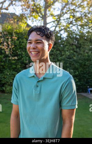 Asiatischer Mann lächelt, während er auf dem Garten an der dichten Hecke steht und das warme Nachmittagssonnenlicht aufsaugt. Outdoor, Freizeit, Natur, Stockfoto