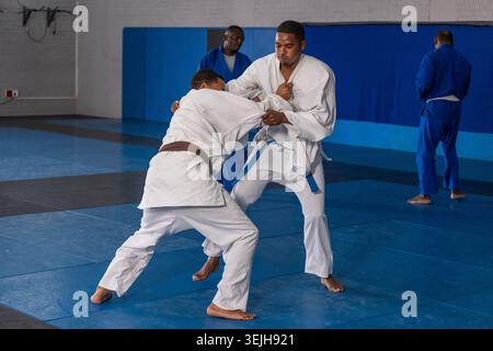 Verschiedene männliche Partner in weißen gis-Greifjacken und Übungswürfen im Dojo auf blauen Matten. Martialarts, Fitness, Traditiona Stockfoto