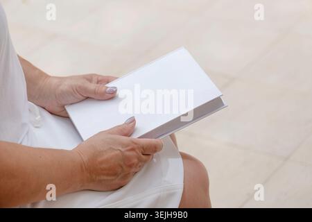 Unerkennbare Frau, die ein leeres Magazin für das Modell hält, auf der Bank sitzt Stockfoto