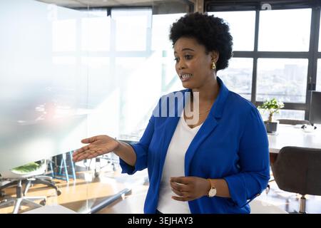 Afroamerikanerin im Blazer, die neben einer Trennwand steht, mit Skyline der Stadt, Kopierraum. Geschäftlich, professionell, modern Stockfoto
