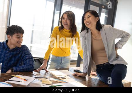 Verschiedene Kollegen prüfen Papierprototypen, Farbmuster im Büro auf dem Tisch mit Smartphone. Zusammenarbeit, Brainstorming, Teamwork, kreative Prozesse Stockfoto