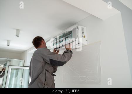 Männlicher Arbeiter, der während der Sommersaison eine Klimaanlage in der Wohnung installiert. Stockfoto