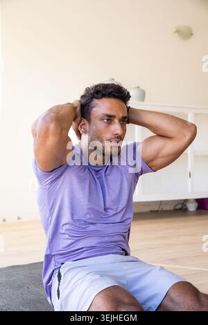 Ein Mann mit 20 Jahren, der Sportkleidung trägt und zu Hause mit Keramikvase Sit-up auf der Trainingsmatte macht. Fitness, Kraft, Wellness, hom Stockfoto